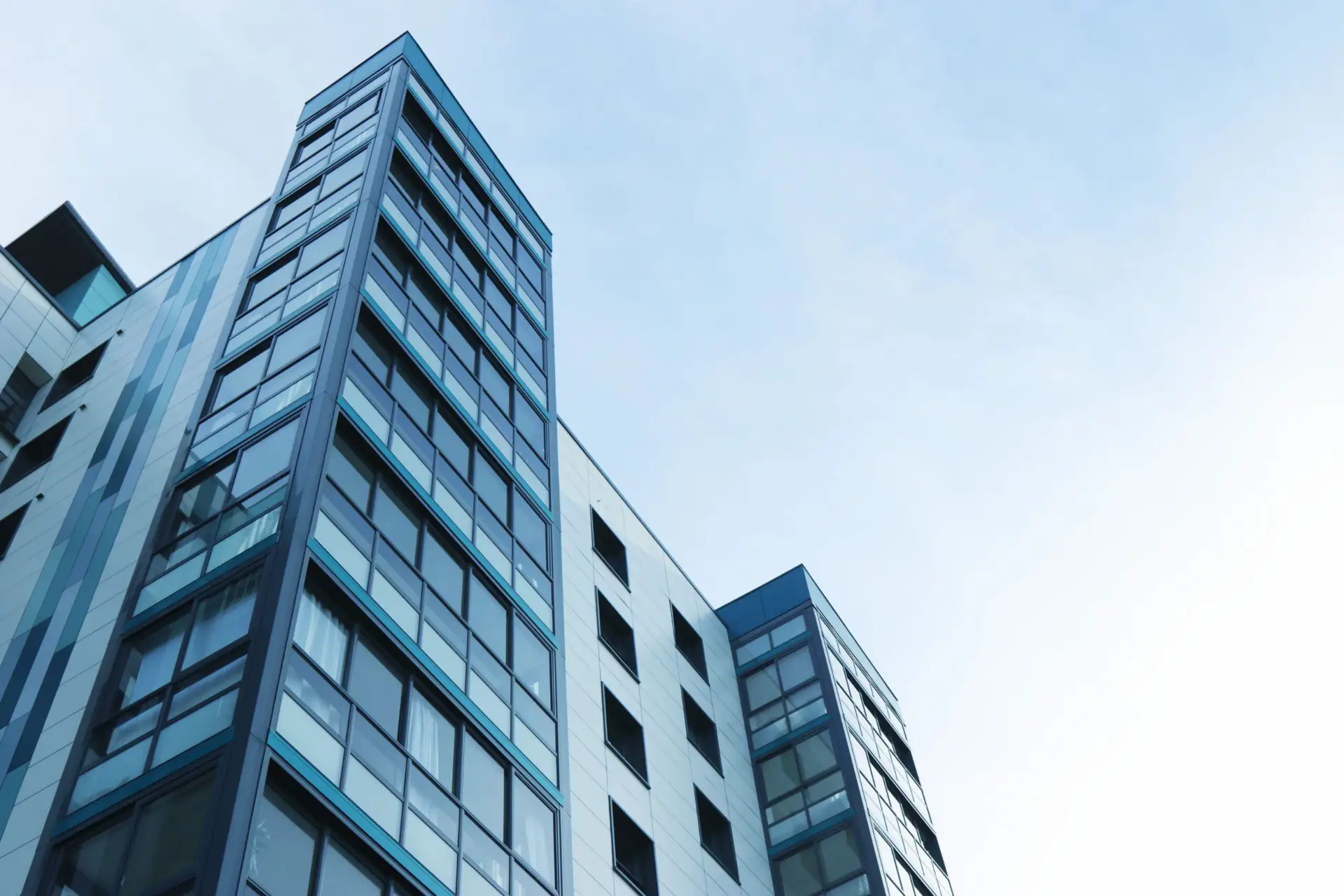 Prédios comerciais altos com fachada envidraçada e janelas em diversos andares, vistos de baixo para cima contra o céu azul, arquitetura urbana moderna.