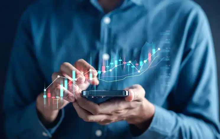 Homem de negócios usando um smartphone com gráficos de análise financeira e tendências de mercado flutuando ao redor, simbolizando investimento digital e tecnologia financeira.