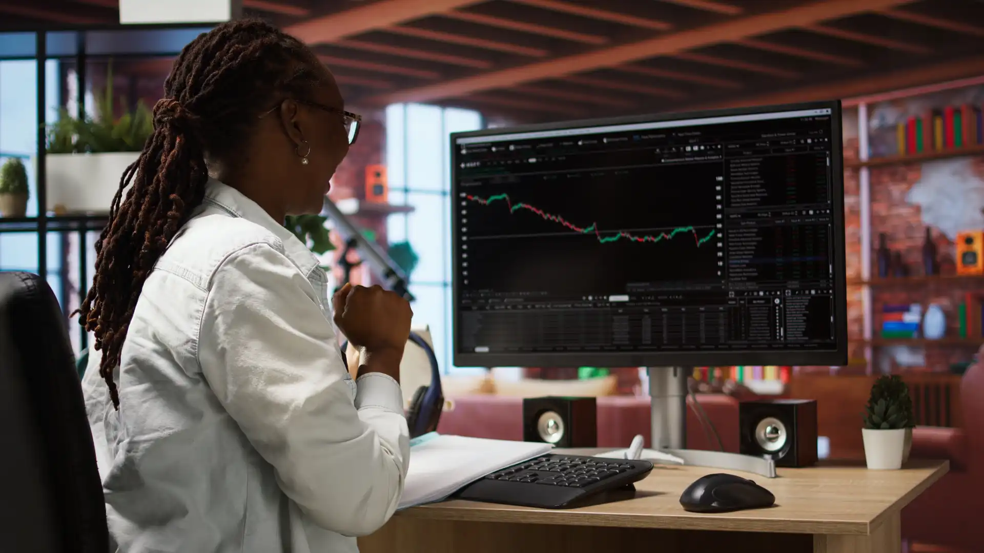 Mulher analisando gráficos de ações no computador em um escritório moderno, focada na análise de mercado financeiro.