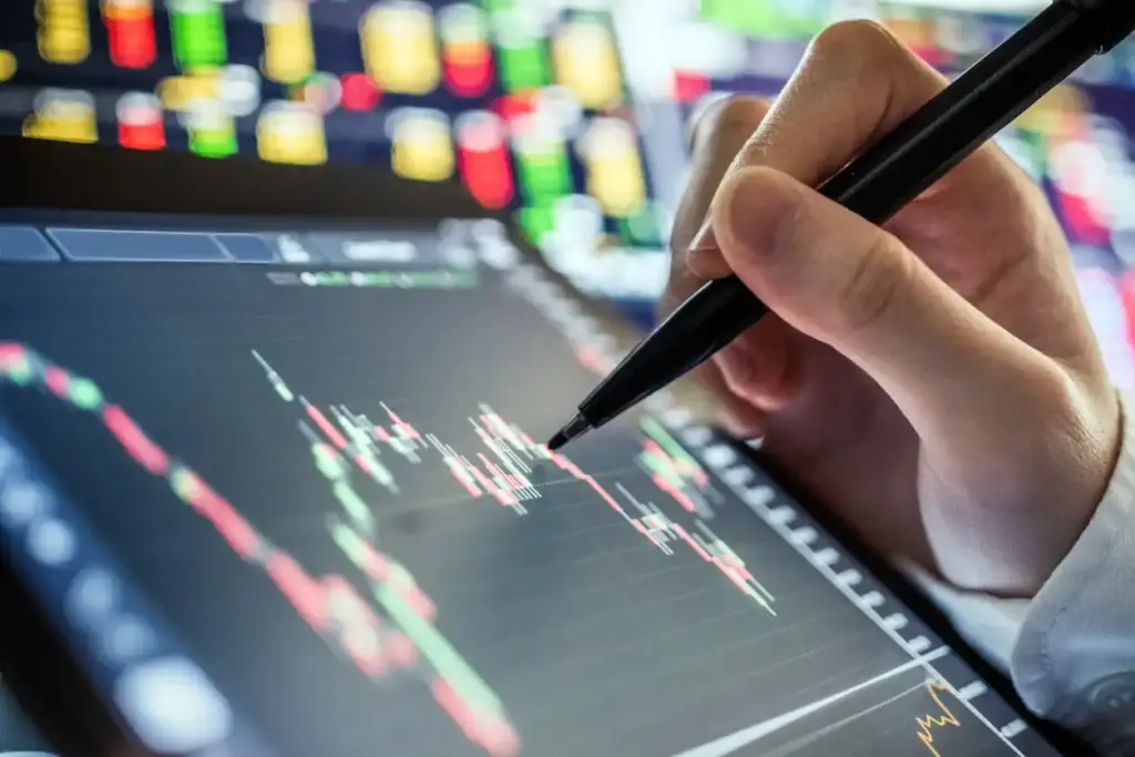 Homem analisando gráficos financeiros em várias telas de computador em um escritório, com foco em mercado de ações.