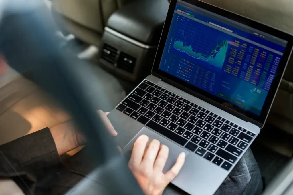 Pessoa analisando gráficos financeiros e tendências de mercado em um laptop, fazendo investimentos ou trades no carro.