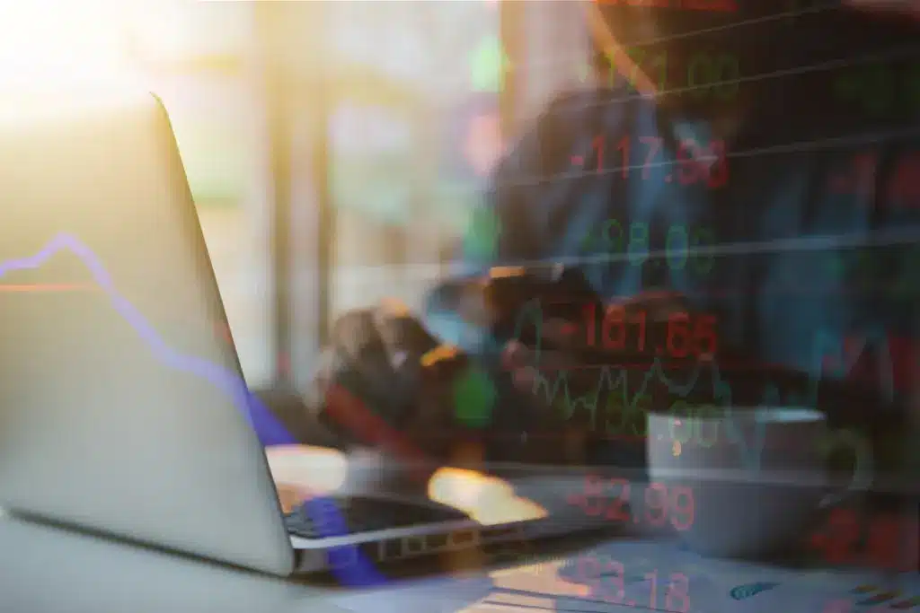 Imagem de uma pessoa analisando gráficos financeiros em um laptop, refletida na tela há números de ações e indicadores de mercado em cores vibrantes, destacando a importância do universo financeiro e dado financeiro.