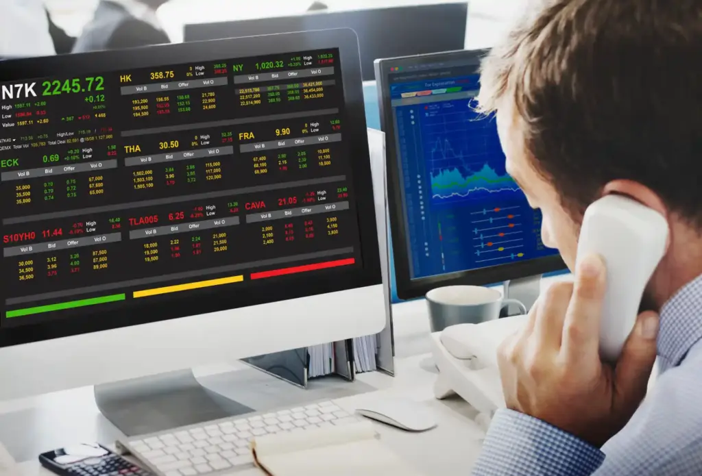Analista de mercado financeiro monitorando ações na bolsa de valores em seu computador, com gráficos e dados de investimentos na tela.