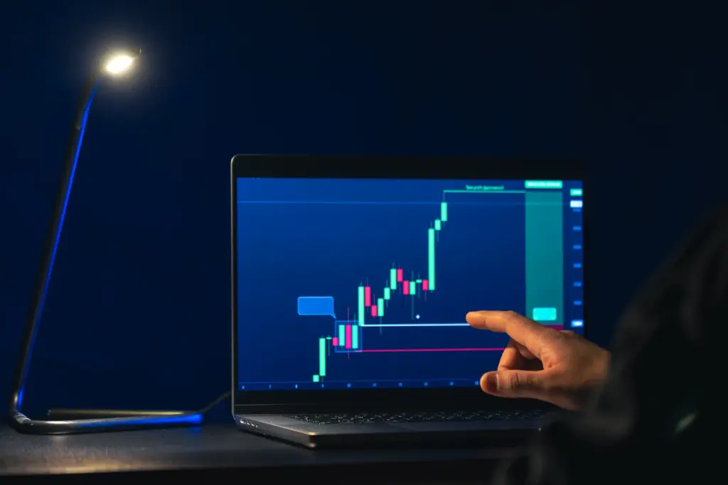 Pessoa analisando gráficos de investimentos em um laptop com uma luminária ao lado, símbolos de crescimento financeiro e trading.