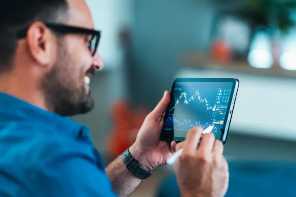 Homem de negócios observando gráficos de ações em um tablet, ilustrando análise financeira e mercado de ações na era digital.