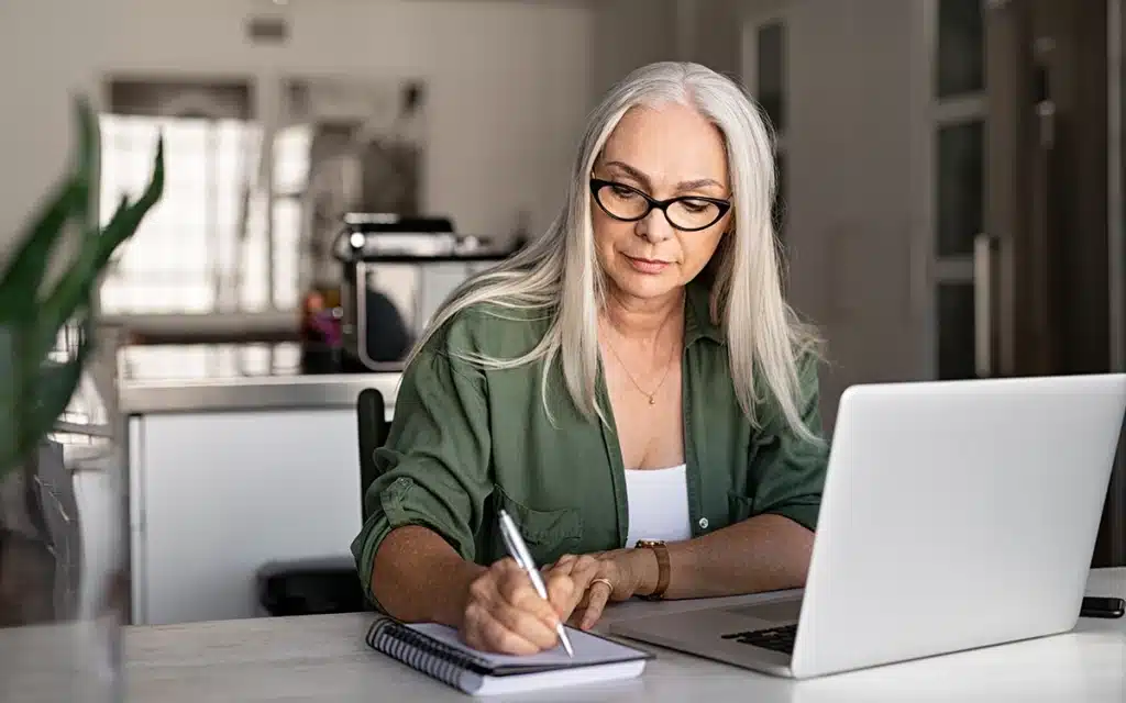 Casal feliz analisando documentos e usando laptop na sala de estar, expressão de satisfação, ambiente acolhedor e iluminado.