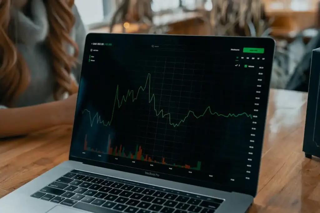 Pessoa analisando gráficos de desempenho financeiro em um laptop MacBook Pro durante uma reunião de negócios em um ambiente de coworking