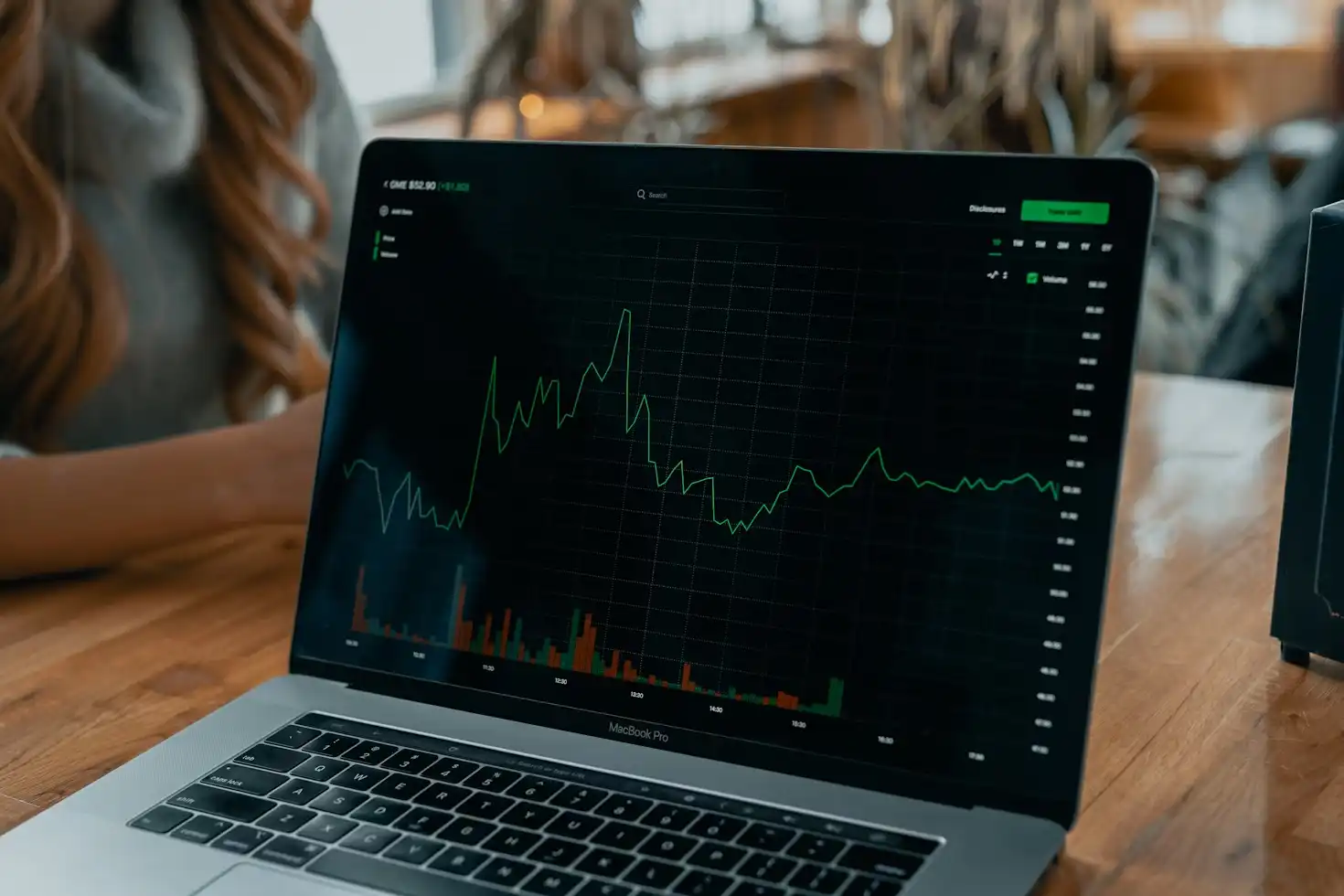 Pessoa analisando gráficos de desempenho financeiro em um laptop MacBook Pro durante uma reunião de negócios em um ambiente de coworking
