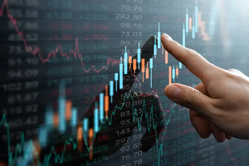 Pessoa apontando para um gráfico de ações ou investimento financeiro digital com linhas de tendência e números, indicando crescimento no mercado financeiro.