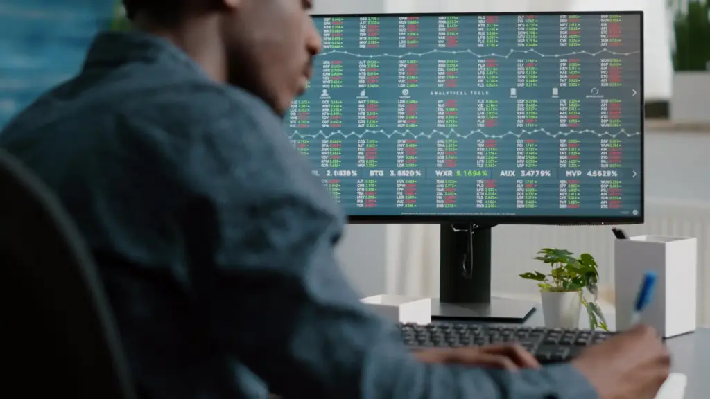 Pessoa observando tela de monitor com gráficos de criptomoedas, indicando análise de mercado financeiro e investimentos digitais.