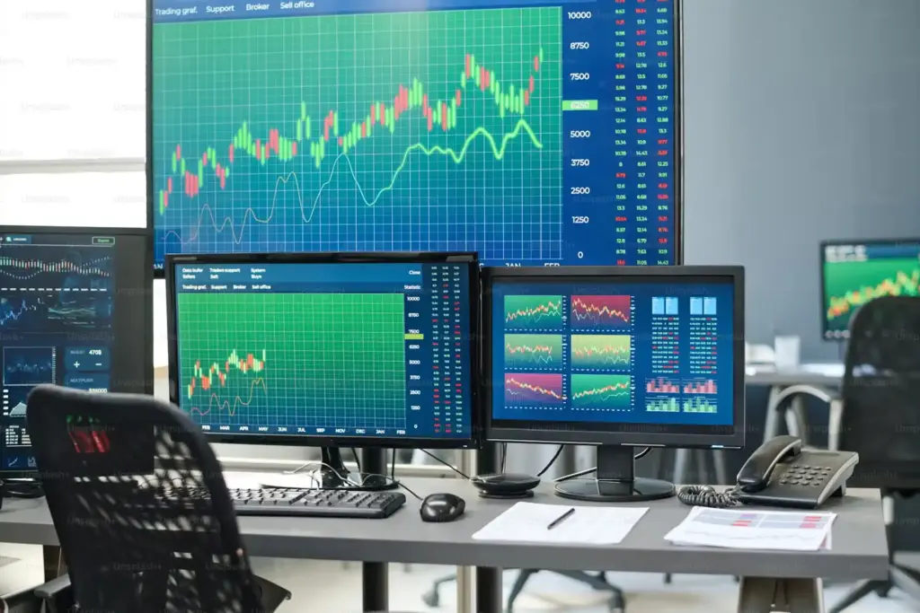 Sala de negociação com múltiplos monitores exibindo gráficos de ações, indicadores financeiros e tendências de mercado, essencial para investidores