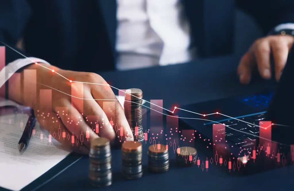 Homem de negócios com pilhas de moedas e gráficos financeiros, simbolizando investimento e crescimento financeiro.