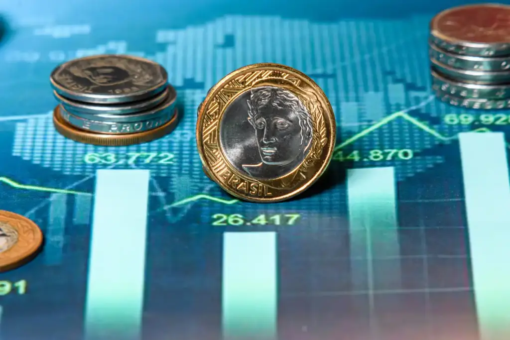 Imagem mostrando moedas brasileiras e um gráfico financeiro de fundo, destacando o movimento do mercado e crescimento econômico.