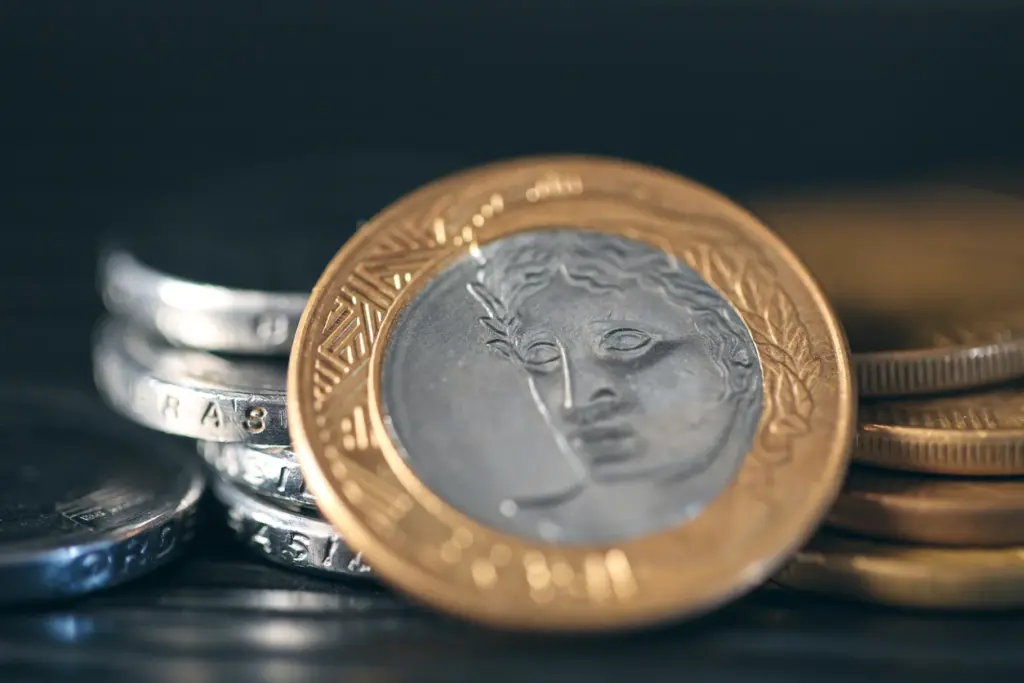 Imagem de moedas de euro empilhadas, incluindo uma de 2 euros com o desenho de uma figura clássica. A imagem destaca o valor e o design das moedas.