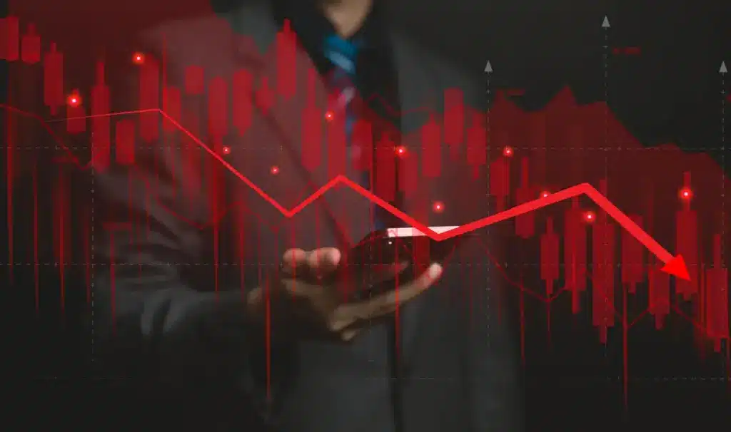Imagem de um analista financeiro ou investidor, com gráficos de queda de ações e indicadores econômicos, representando crise ou queda no mercado financeiro.