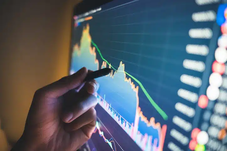 Imagem de uma pessoa analisando gráficos de ações em uma tela de computador, demonstrando tendências de queda no mercado financeiro.