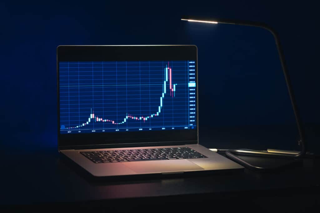 Notebook exibindo gráfico de velas de mercado financeiro em alta, com iluminação escura ao fundo, simbolizando trading online, análise de ações e investimentos digitais.