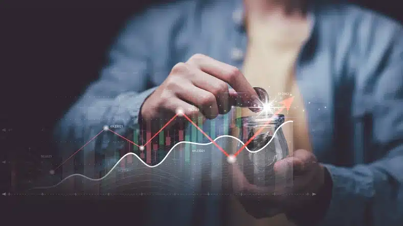 Pessoa segurando moedas de dinheiro com gráficos financeiros digitais e indicadores de crescimento elevados, representando investimento e economia em PT-BR.