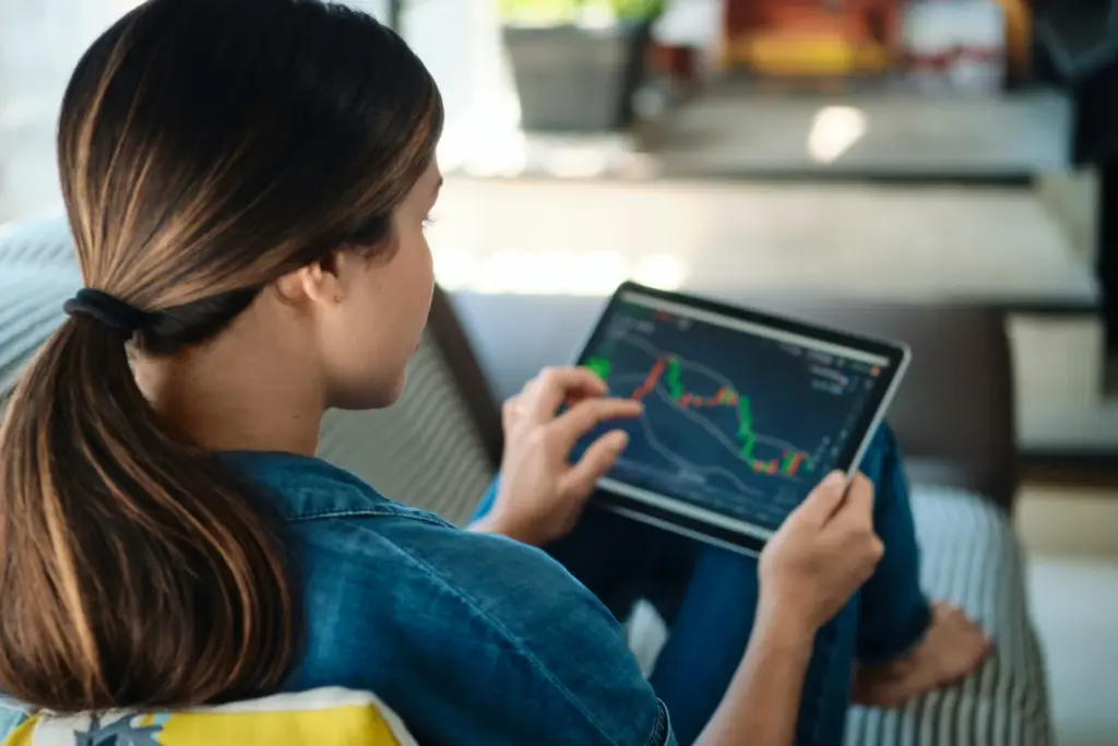 Mulher analisando gráfico de ações no tablet em ambiente interno, destacando o uso de tecnologia para investimentos financeiros.
