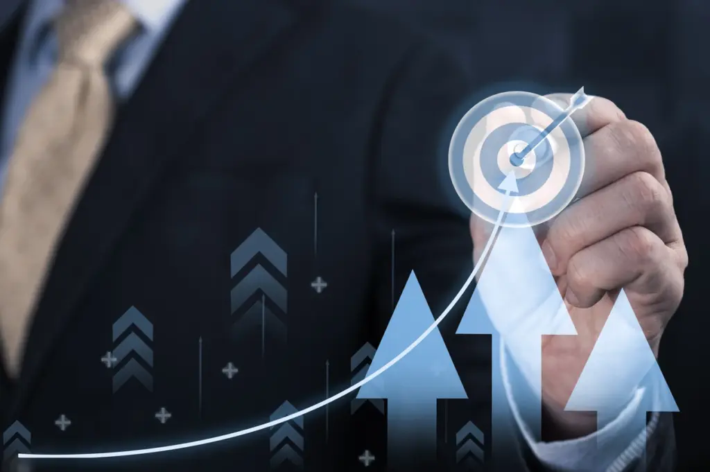 Mão masculina acionando gráfico com seta ascendente e ícones de indicadores, simulando crescimento e metas, com sobreposição de figura de sucesso em contexto corporativo