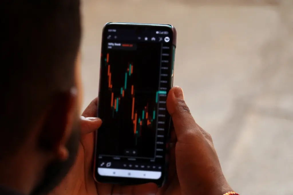 Pessoa analisando gráficos de ações no smartphone, com foco em tendências de mercado financeiro e investimentos em bolsa de valores.