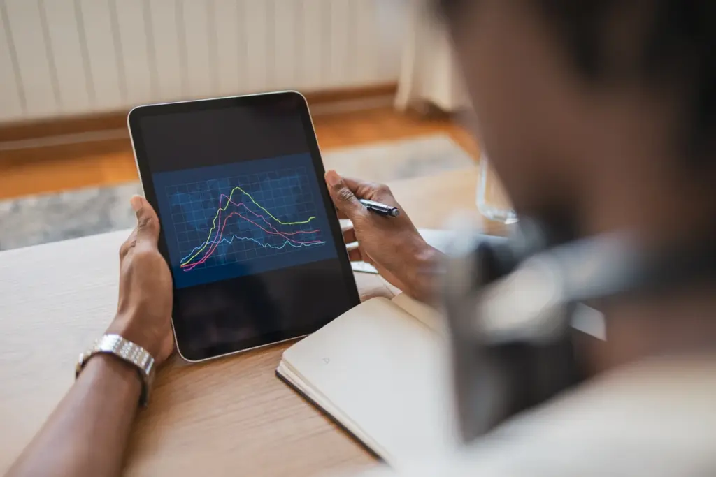 Pessoa analisando gráfico de dados em tablet, indicando análise de métricas e desempenho, com caderno ao lado, focado em tecnologia e negócios