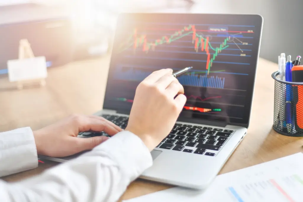 Pessoa analisando gráficos de ações em um laptop, com foco em investimentos financeiros e mercado de ações.