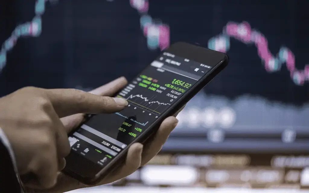 Pessoa analisando gráficos de mercado de ações no smartphone em ambiente de negócios.