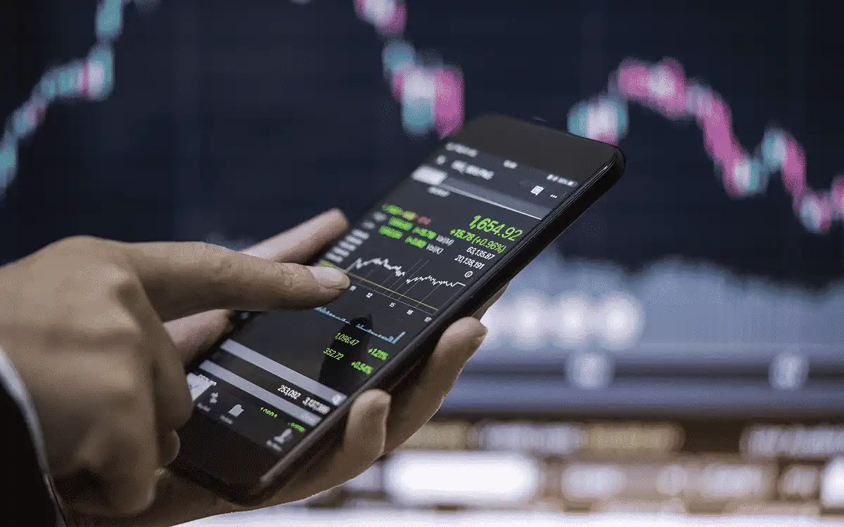Pessoa analisando gráficos de mercado de ações no smartphone em ambiente de negócios.