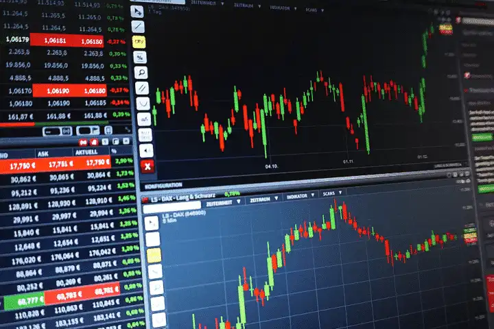 Imagem de gráficos de mercado financeiro mostrando alta e baixa de ações em uma tela de computador, com destaque para números, velas e tendências de investimento.