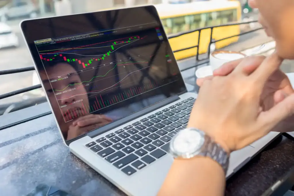 Homem analisando gráficos de ações em um laptop, simbolizando investimento e análise financeira.