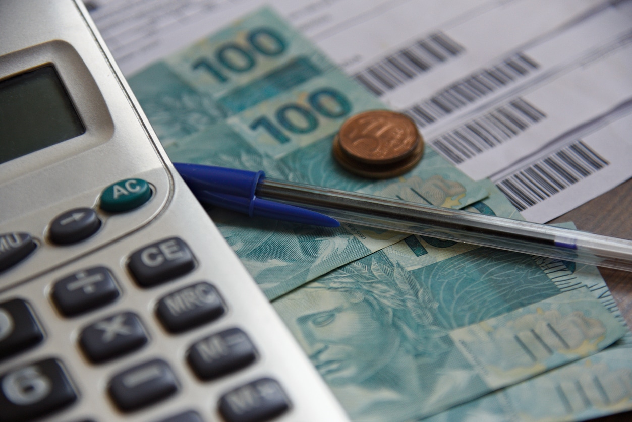 Cédulas de real brasileiro ao lado de uma calculadora, com referência à taxa Selic.
