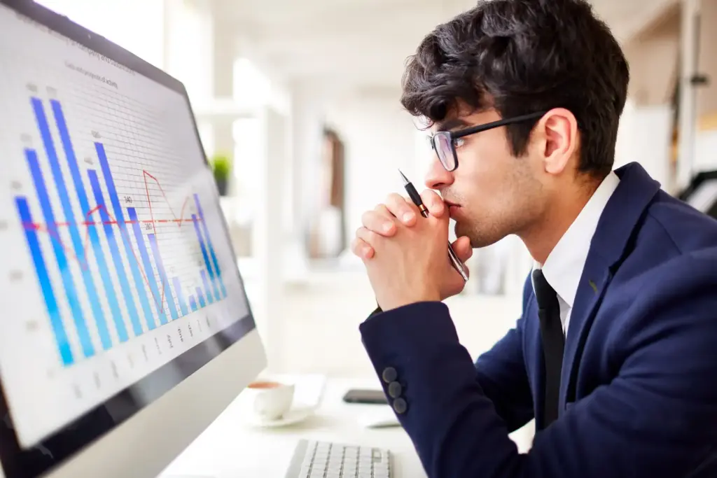 Homem sério analisando gráficos financeiros em um computador, representando análise de dados e estratégias de negócios.