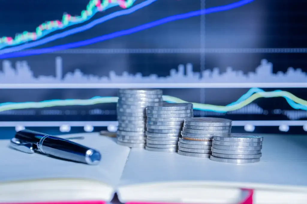Imagem de moedas empilhadas em um ambiente de análise financeira, com gráficos de desempenho de ações ao fundo, destacando crescimento e investimentos.