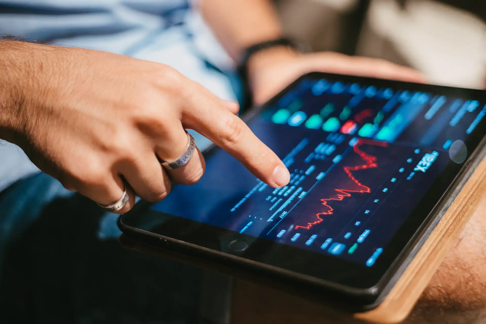 Pessoa analisando gráficos e dados financeiros em um tablet, envolvendo análise de mercado e tendências econômicas.