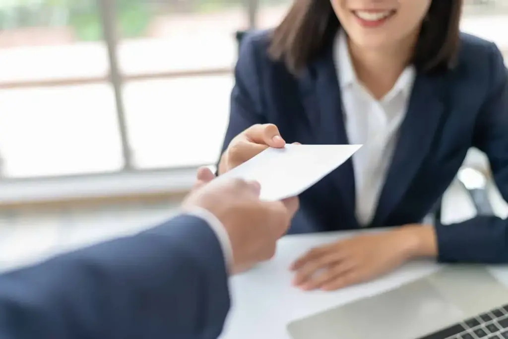 Pessoa entregando um documento para uma mulher sorridente em um ambiente de escritório, simbolizando oferta ou assinatura de contrato, com foco na negociação.