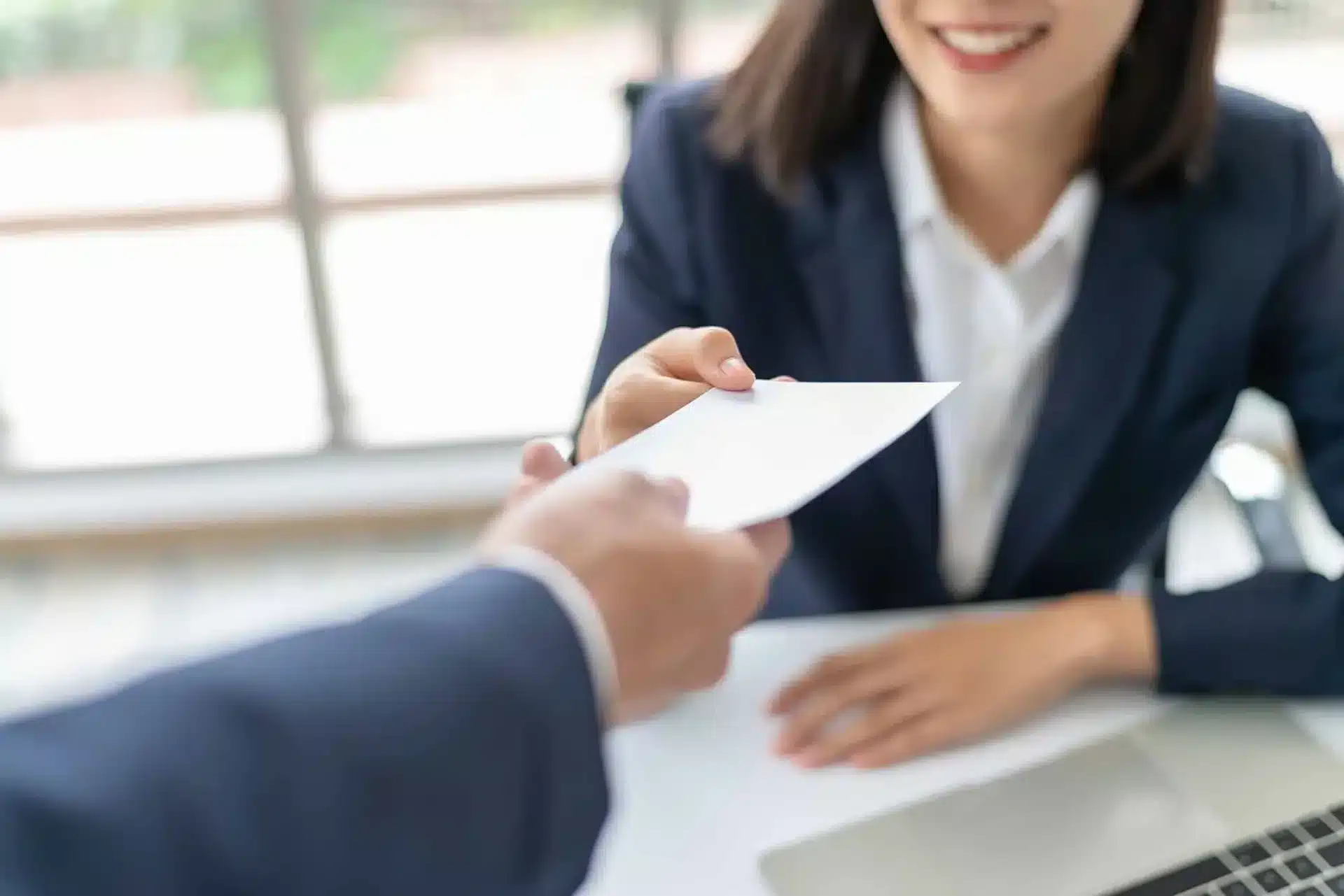 Pessoa entregando um documento para uma mulher sorridente em um ambiente de escritório, simbolizando oferta ou assinatura de contrato, com foco na negociação.