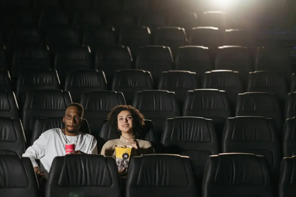 Duas pessoas assistindo a um filme em sala de cinema vazia, com assentos de couro preto e iluminação suave.