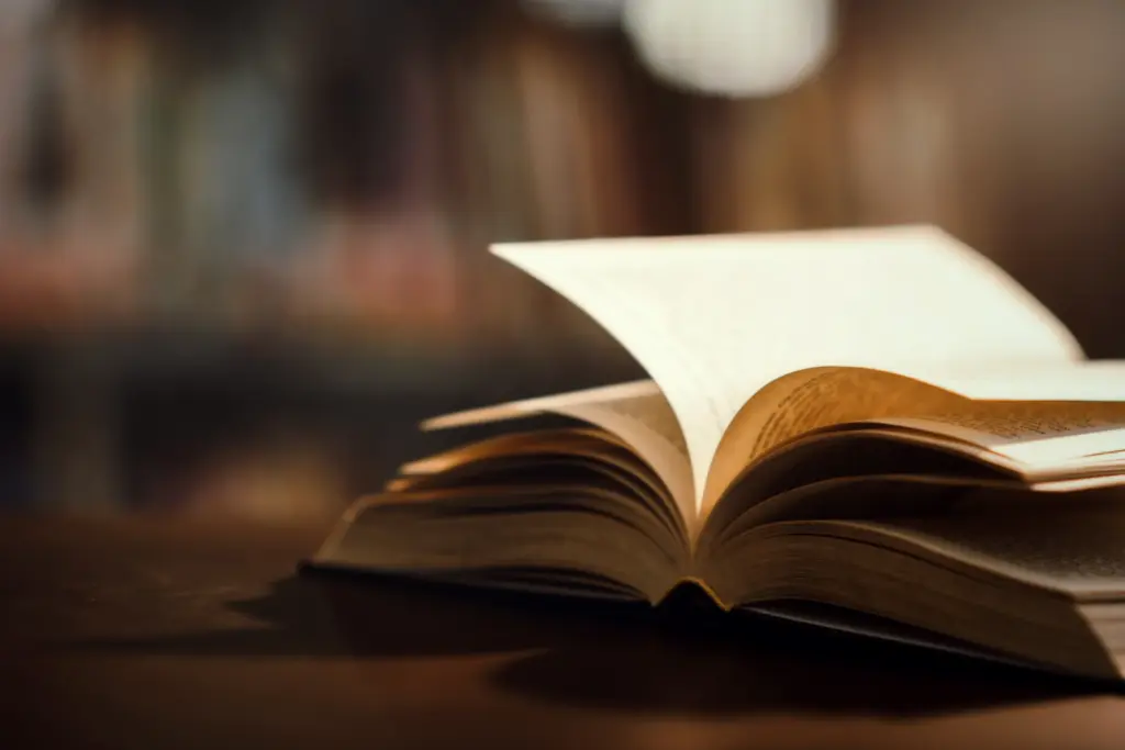 Livro aberto em uma mesa de madeira com fundo desfocado. Cena tranquila e ideal para quem busca leitura ou estudo. Imagem com foco na leitura e conhecimento.